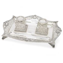 Late Victorian silver desk stand, of rectangular form, with shaped and pierced, oblique gadrooned rim, upon four paw feet, the central tray with two pen holders and two reserves holding cut glass silver topped inkwells, hallmarked William Hutton & Sons Ltd, Sheffield 1900, tray W23cm