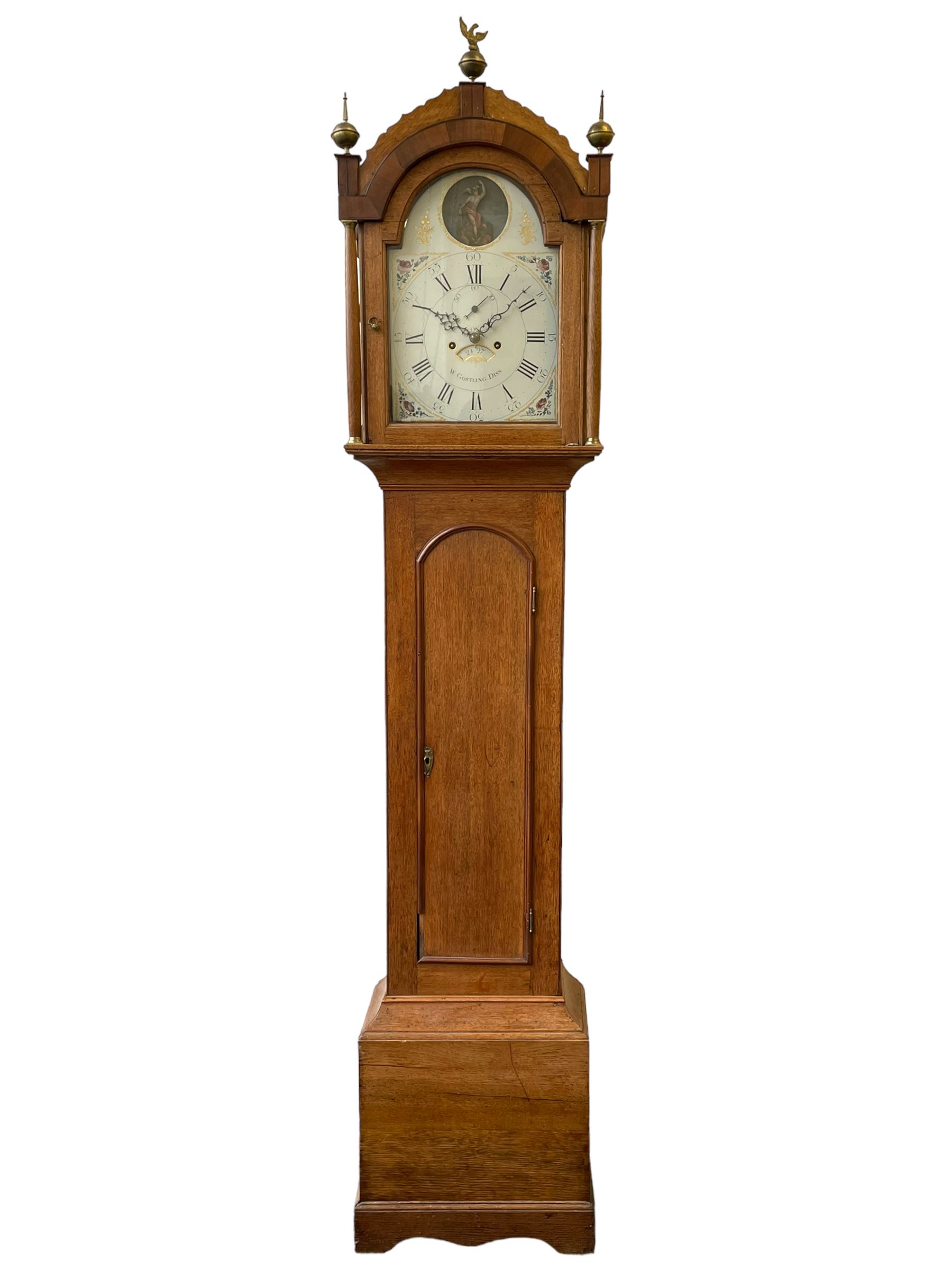William Gostling of Diss  (Norfolk)-  Late 18th century 8-day oak longcase clock c1780-90, break arch top with scalloped cresting and three brass finials, glazed break arch hood door flanked by turned pilasters with brass capitals, trunk with a long trunk door and rounded top on a square plinth with an applied and shaped skirting, early painted Wilson of Birmingham dial with Roman numerals and five minute Arabic's, matching steel hands and second pointer, arched square ended calendar aperture with date disc behind, floral spandrels within gesso borders and a painted rocking automaton representing Mercury to the break arch, dial pinned via a false plate to a weight driven rack striking movement with a recoil anchor escapement, striking the hours on a cast bell. With pendulum weights and key. 
William Gostling (II) is recorded as working in Diss from 1774 to 1797, succeeded by widow Anne and son George . The dial of this clock is illustrated and discussed in detail in M.F. Tennants book 