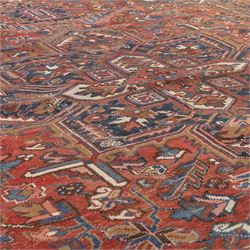 Persian Heriz carpet, red ground with large central geometric medallion, angular flowering branches and stylised foliate decoration, within a broad dark blue floral border and narrow guard stripes
