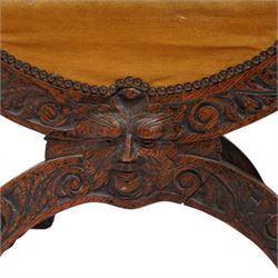 Victorian heavily carved oak X-framed throne chair, the cresting rail carved with mask and curling foliage, upholstered in mustard fabric, the arms and frame carved with scrolling foliage, united by turned stretchers 
