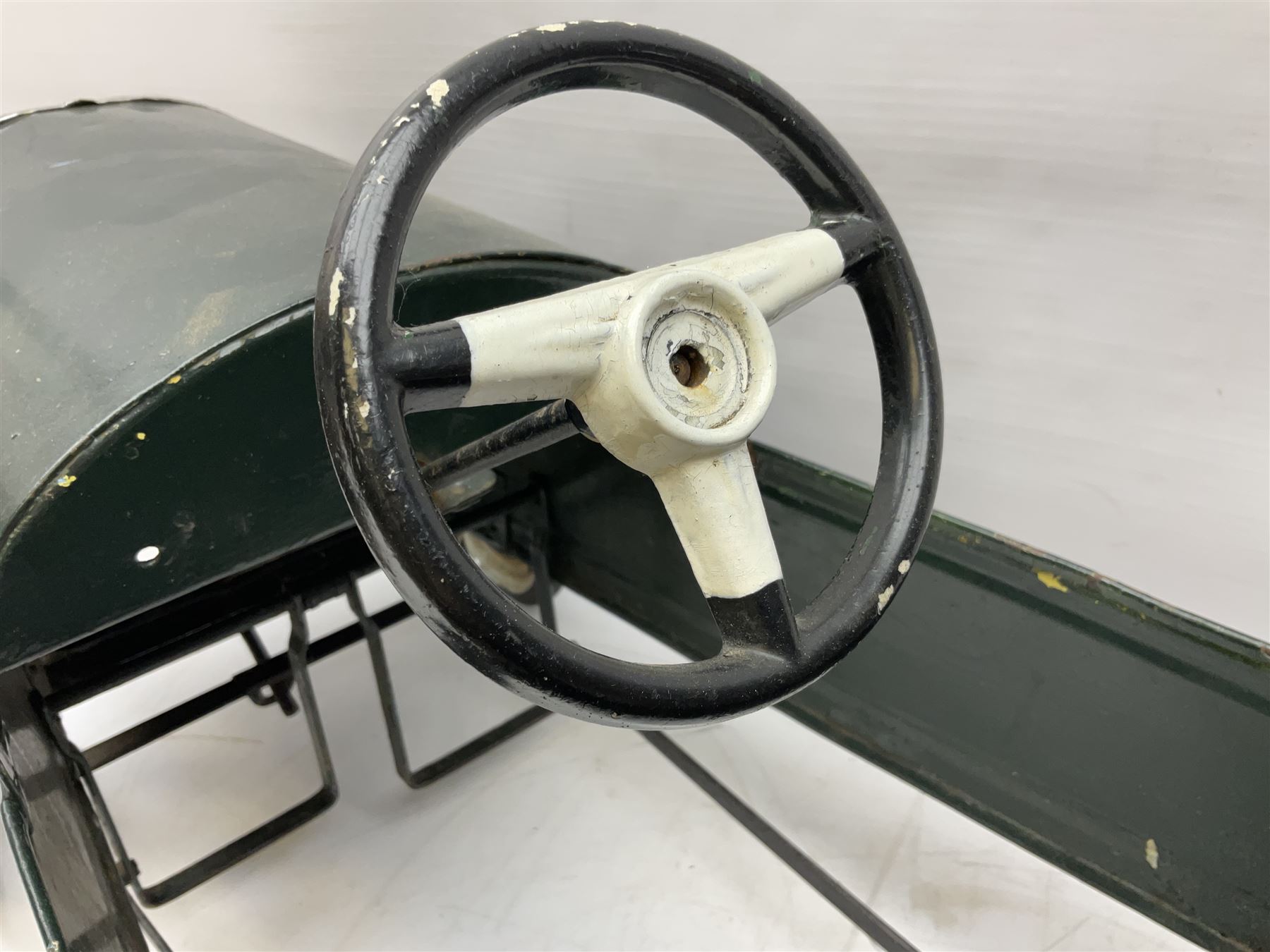 Mid 20th century pressed steel pedal car, the body painted in dark green fitted with pretend radiator to the bonnet, with spoked wheels and rubber tyres, the interior with pedals and steering wheel, L70cm