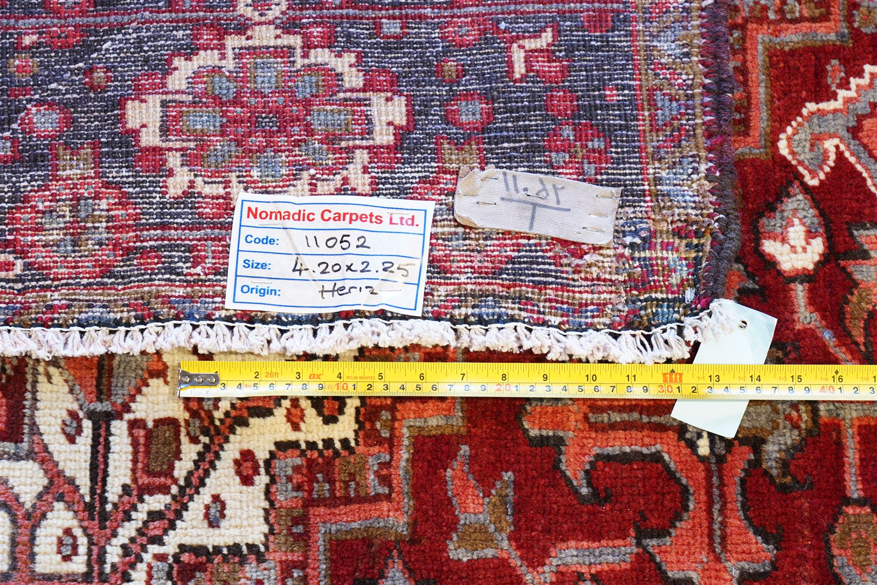 North West Persian Heriz hand-knotted carpet, brick red field with a large central angular star medallion with pendants surrounded by stylized geometric palmettes, serrated leaves and tribal motifs,, ivory corner spandrels, field enclosed by a dark indigo main border of stylize rosettes and angular vine motifs between multiple guard stripes, with cotton fringe ends 