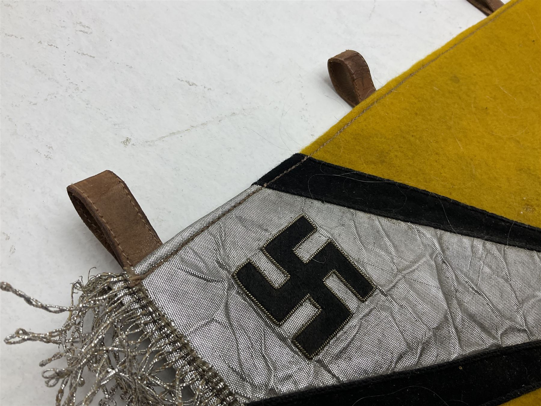 Two replica German Luftwaffe trumpet banners, one heavily silver wire embroidered with Luftwaffe eagle in a wreath, on an amber, white and black rayed background, , with silver wire tasselled border and four leather hanging loops, approx. 50 x 49cm; the other slightly larger heavily gold wire embroidered with the Luftwaffe eagle on a plain amber ground with gold wire tasselled border and two hanging loops (2)