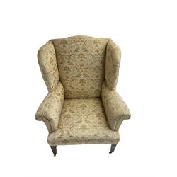 19th century wingback armchair, upholstered in ivory fabric with green and coral foliate pattern, scrolled arms with sprung seat, raised on mahogany tapering feet united by H stretcher, on brass castors 