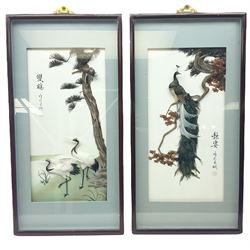 Two Oriental framed feather art pictures, one depicting a peacock upon a branch, the other a pair of cranes under a tree, H70cm