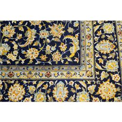 Central Persian Kashan hand-knotted carpet, deep indigo field with a densely all-over arrangement of scrolling floral vines, palmettes, and flowering sprays, in soft ivory, pale blue, and warm gold tones, principal ivory border with a continuous meandering vine of stylized palmettes, and floral motifs, flanked by multiple narrow guard borders, with cotton fringe ends 