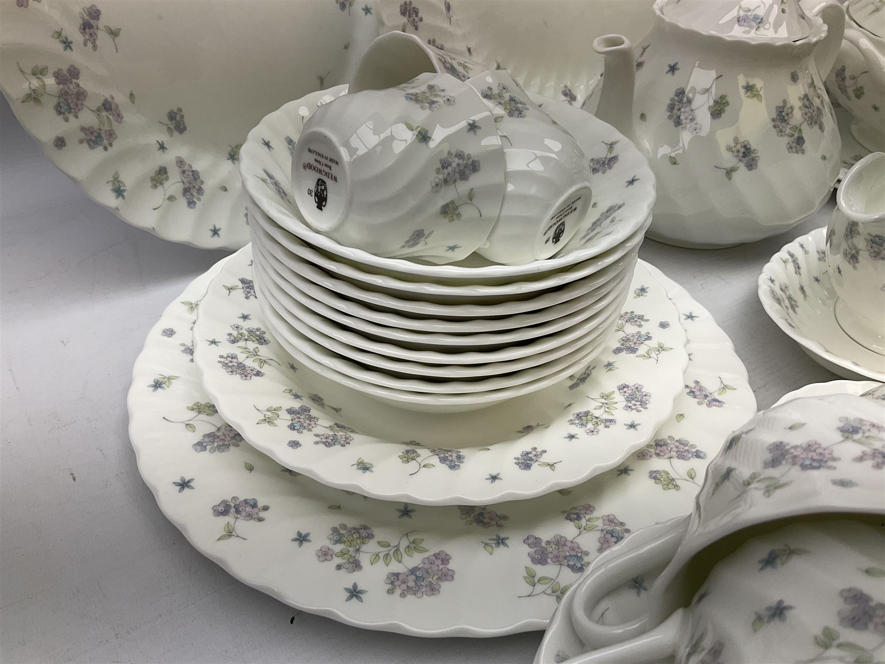 Wedgwood tea and dinner service decorated in the ‘April Flowers’ pattern, to include nine bowls, seven teacups and saucers, three coffee cups and saucers, sauce boat and stand, lidded tureen, covered sucrier and another smaller, oval serving plate, twelve side plates, teapot, four dinner plates, jug and shallow bowl