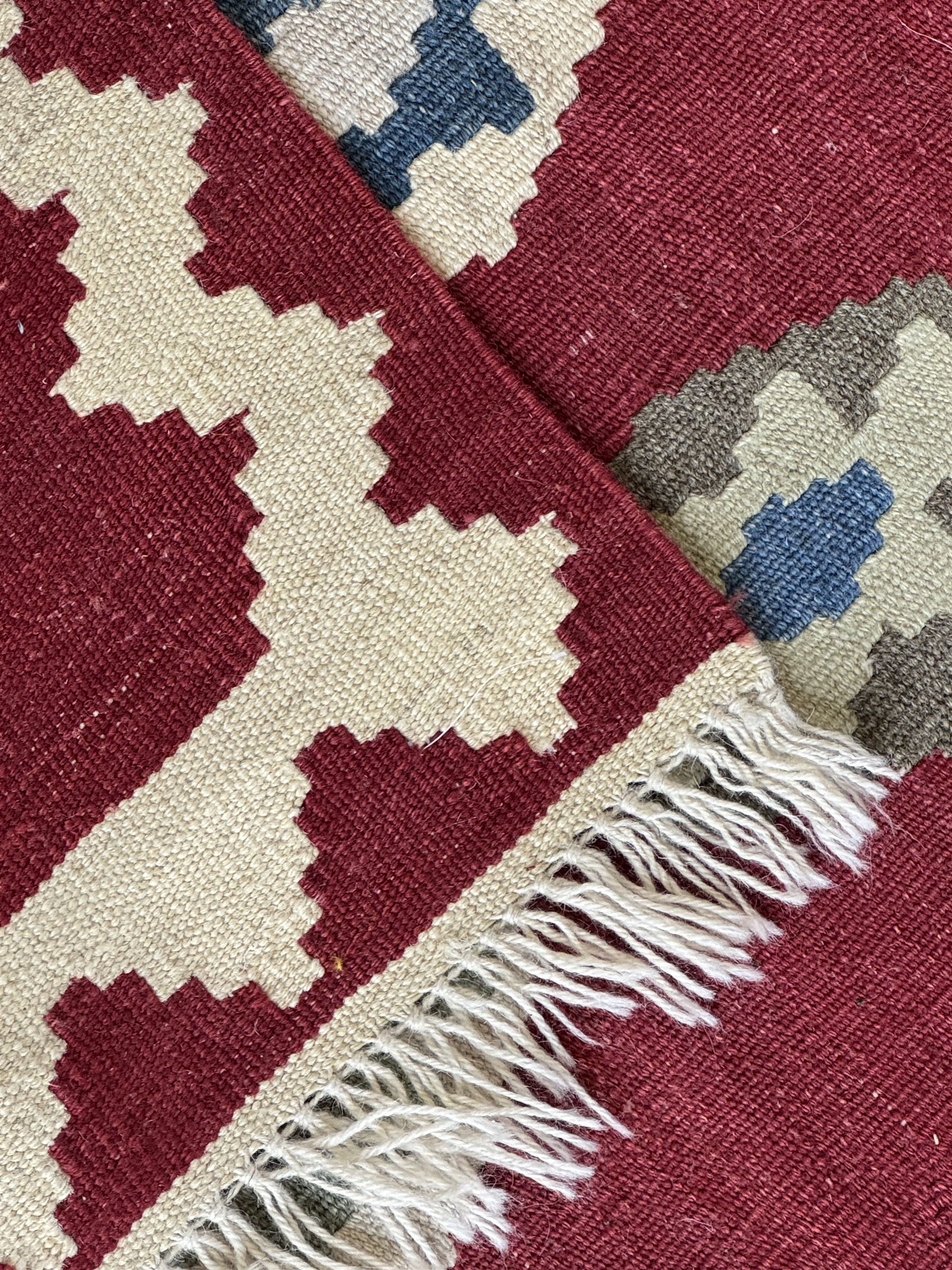 Handwoven wool Kilim rug of rectangular form with cream fringe, the red ground decorated with repeated multicoloured hexagonal medallions within a cream stepped border