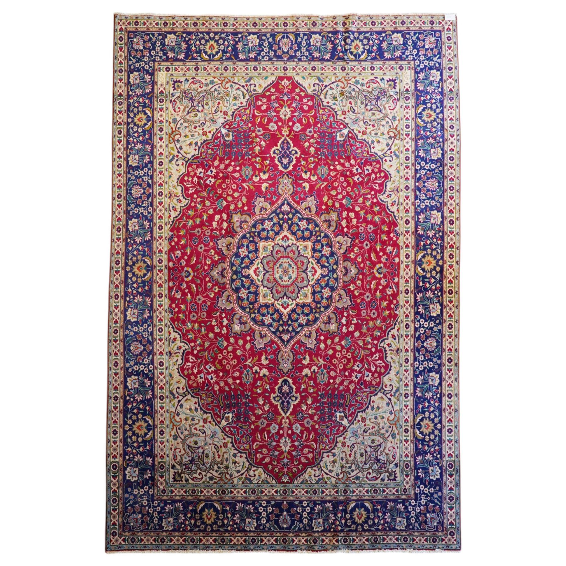 North West Persian Tabriz hand-knotted carpet, madder red field with a central cusped medallion issuing radiating pendants and an all-over design of scrolling arabesques, palmettes and flowering vinery enclosed by conforming spandrels, indigo main border of meandering floral vines and stylized palmettes, flanked by narrow guard stripes, cotton fringe ends 