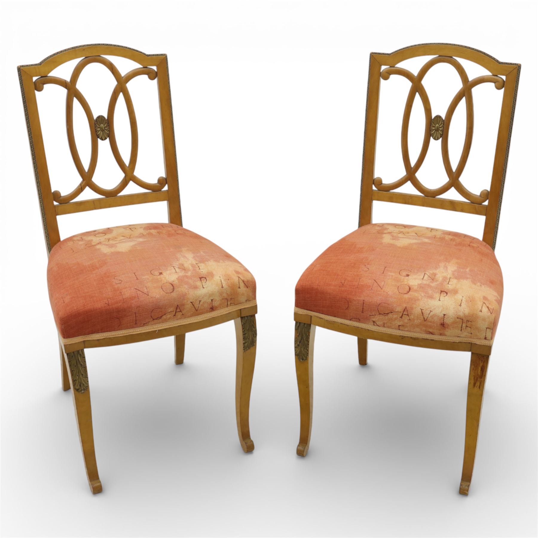 Edwardian pair of satinwood side chairs, each with shaped crest rail above an intertwining oval pierced splats centred by a floral patera, upholstered drop-in seats, raised on cabriole supports with applied floral mounts to the knees