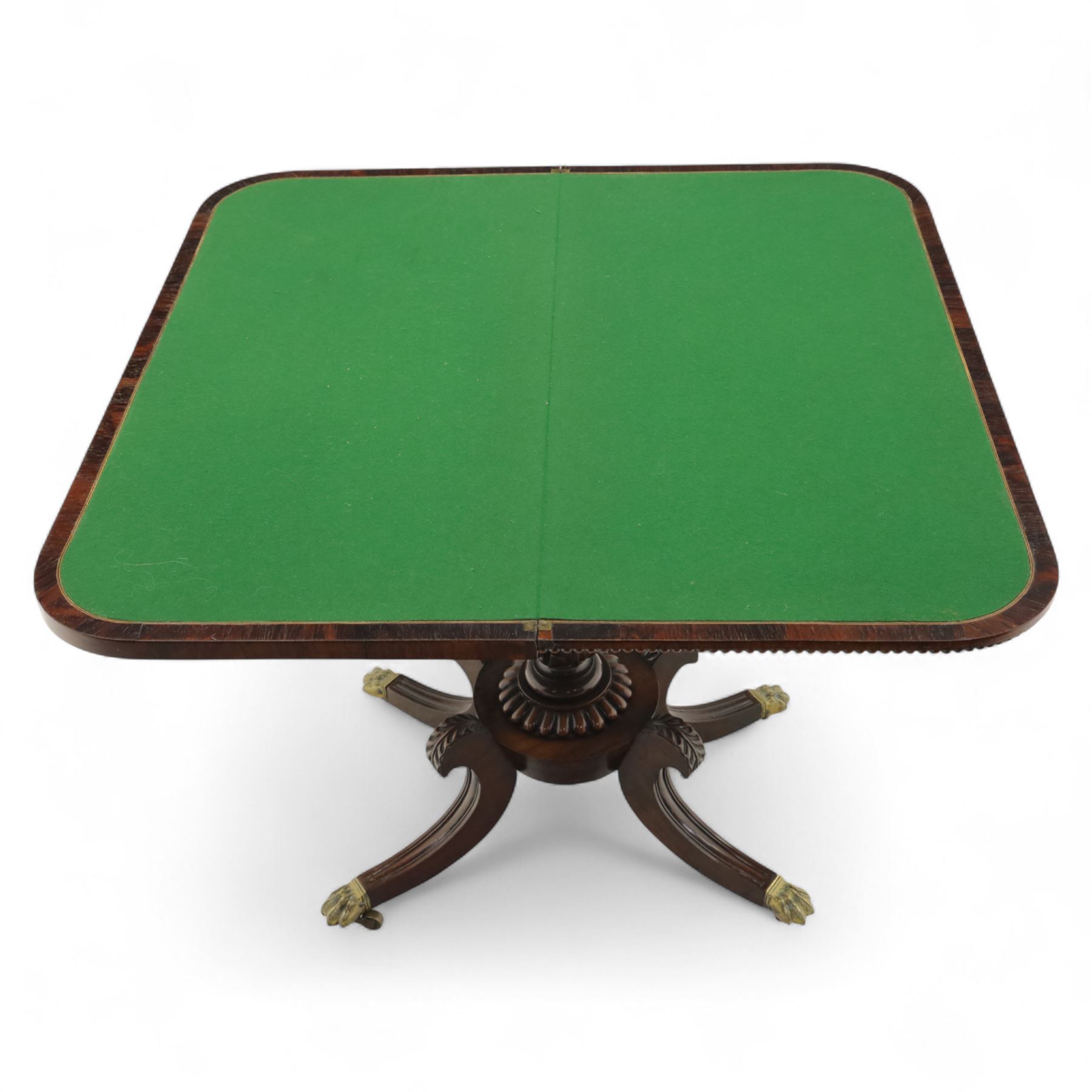 Regency rosewood fold over card table, the rectangular top with rounded corners and gadrooned edge opening to reveal a green baize lined interior, raised upon convex lobbed and acanthus pedestal and four fluted sabre legs, terminating in brass lion paw feet and castors