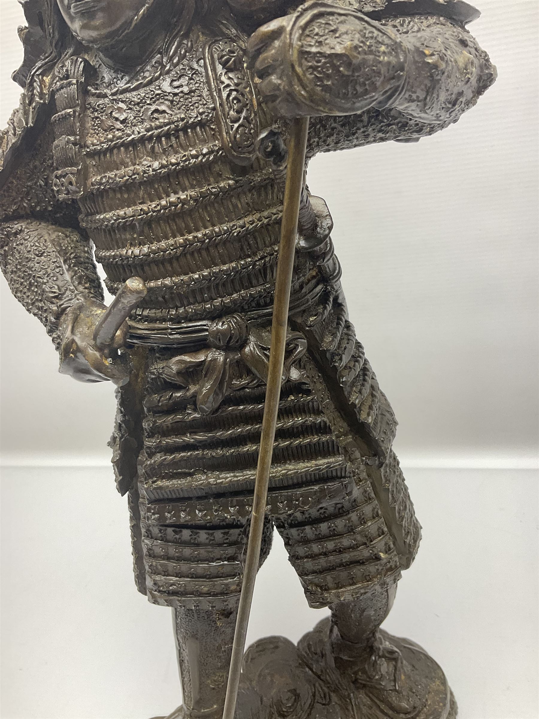 Bronze figure of a samurai standing wearing armour and holding a naginata, upon a rocky base, H48cm