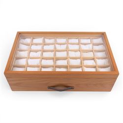 Large wooden watch display case, with glazed lid and spaces for thirty five watches, with drawer beneath containing a collection of leather, metal and other watch straps