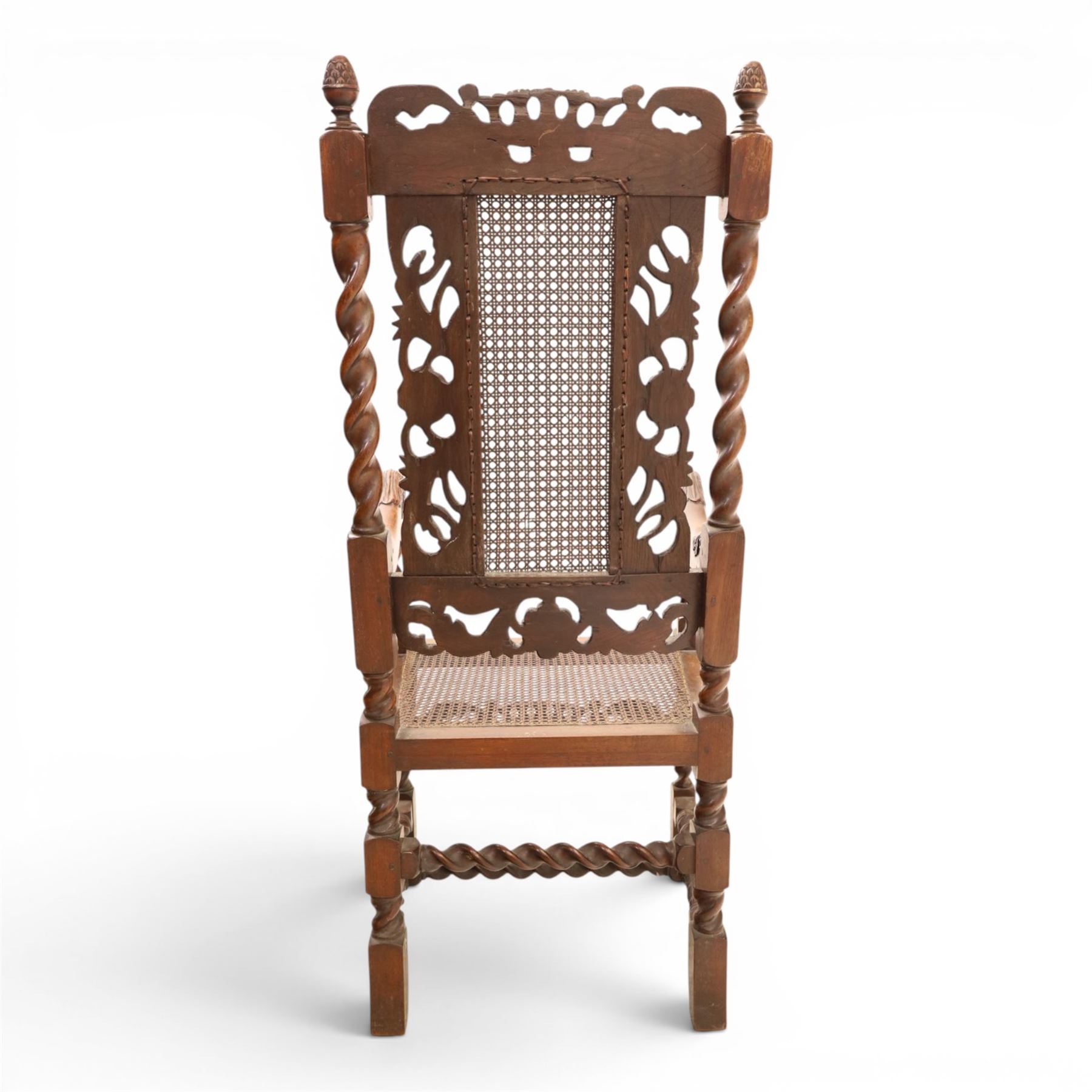 Late Victorian Jacobean Revival oak armchair, the caned back within a pierced and carved foliate frame surmounted by acorn finials, carved scroll arm supports, caned seat, on barley twist supports united by stretchers and carved front rail