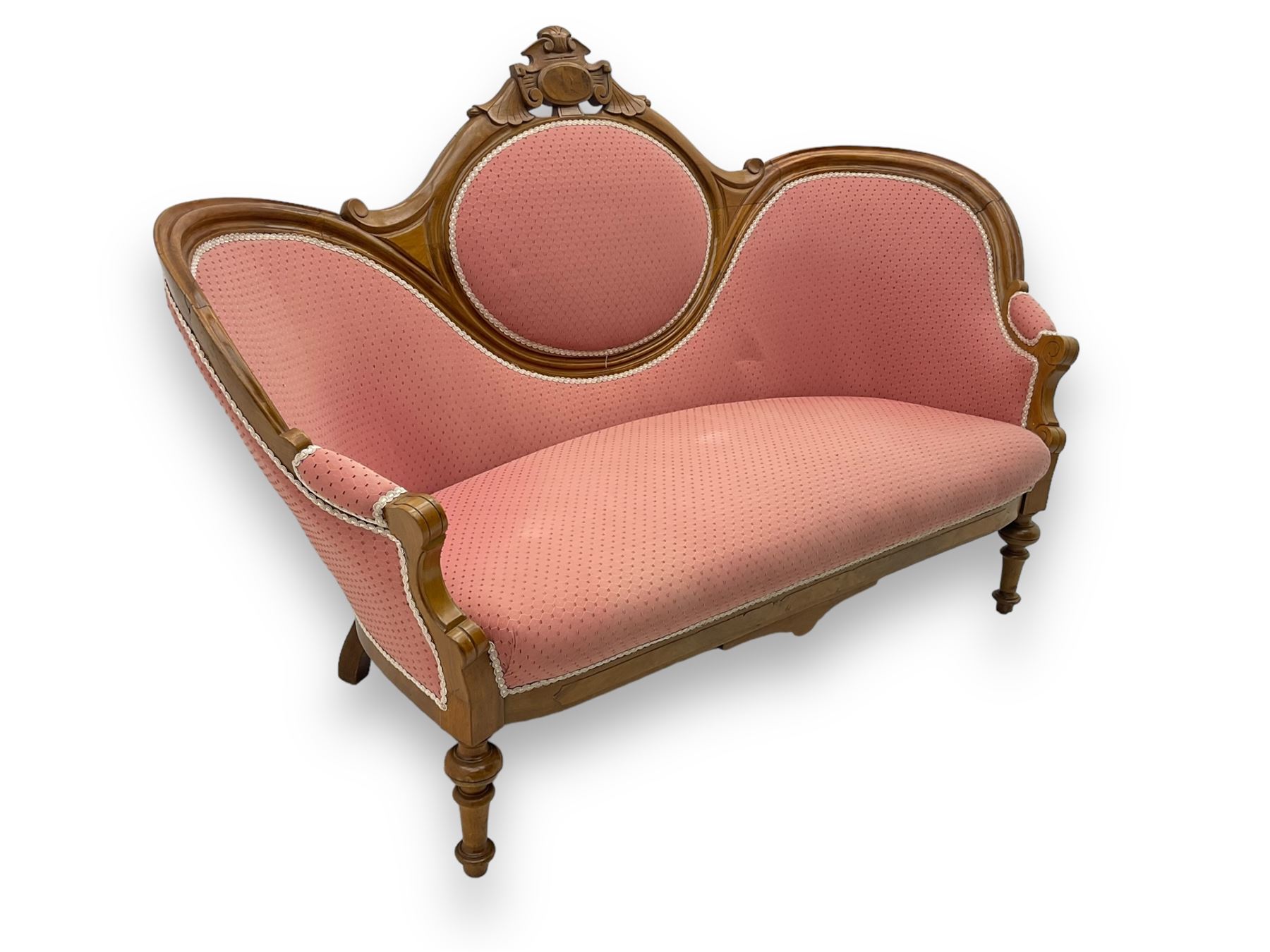 Late Victorian walnut framed double spoon back sofa, shaped crest rail with central carved medallion over curved back with pink upholstery, scrolling arms with additional carvings, on turned supports