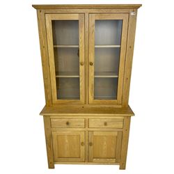 Contemporary light oak bookcase display cabinet, fitted with  two glazed doors enclosing two shelves, above two drawers and cupboards