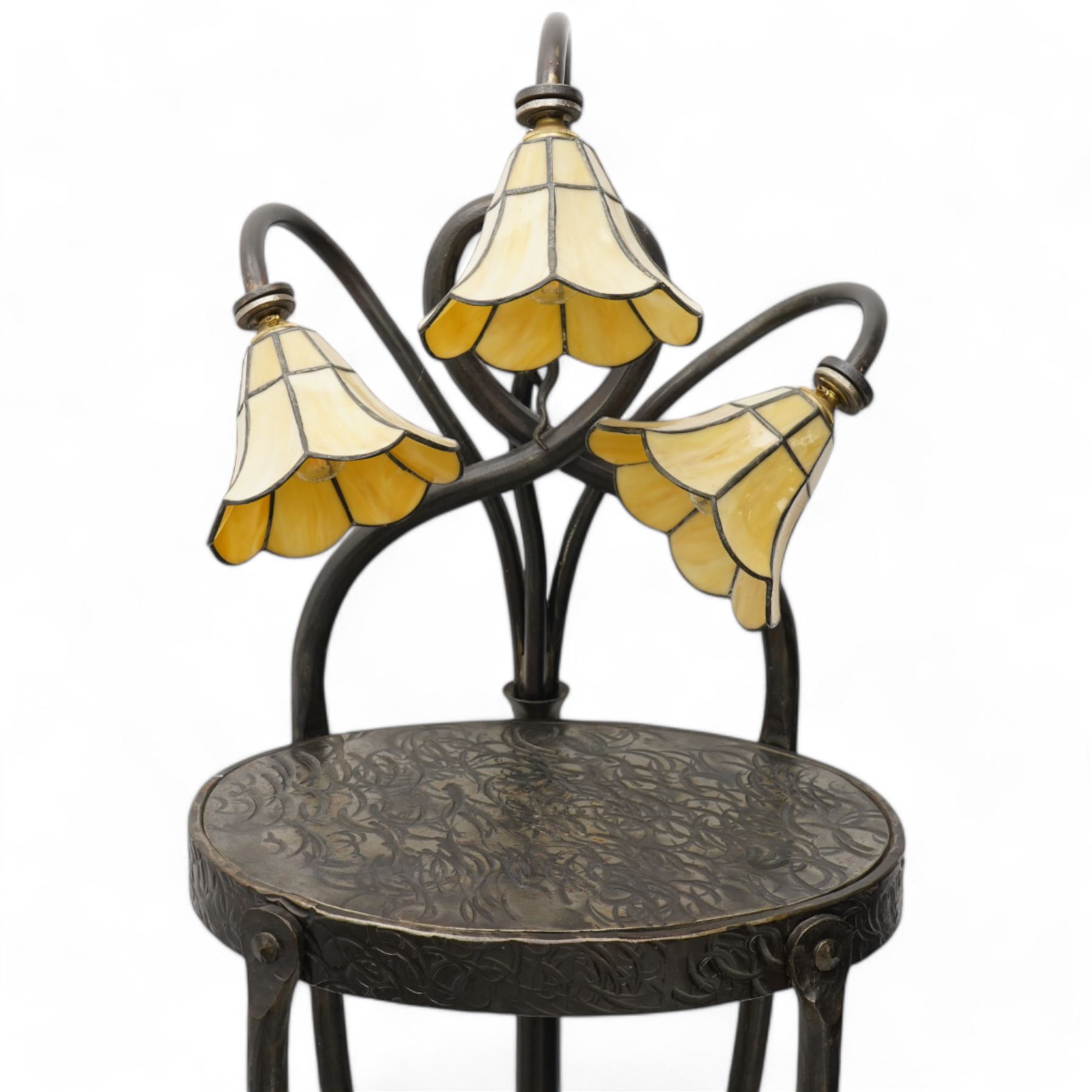 James Godbold - Art Nouveau blacksmith-made wrought iron floor standing lamp table, the round etched metal tabletop decorated with swirling foliage motifs, crowned by three Tiffany design amber glass shades mounted on curved iron stems, raised on four splayed supports united by circular stretcher and terminating in ball feet