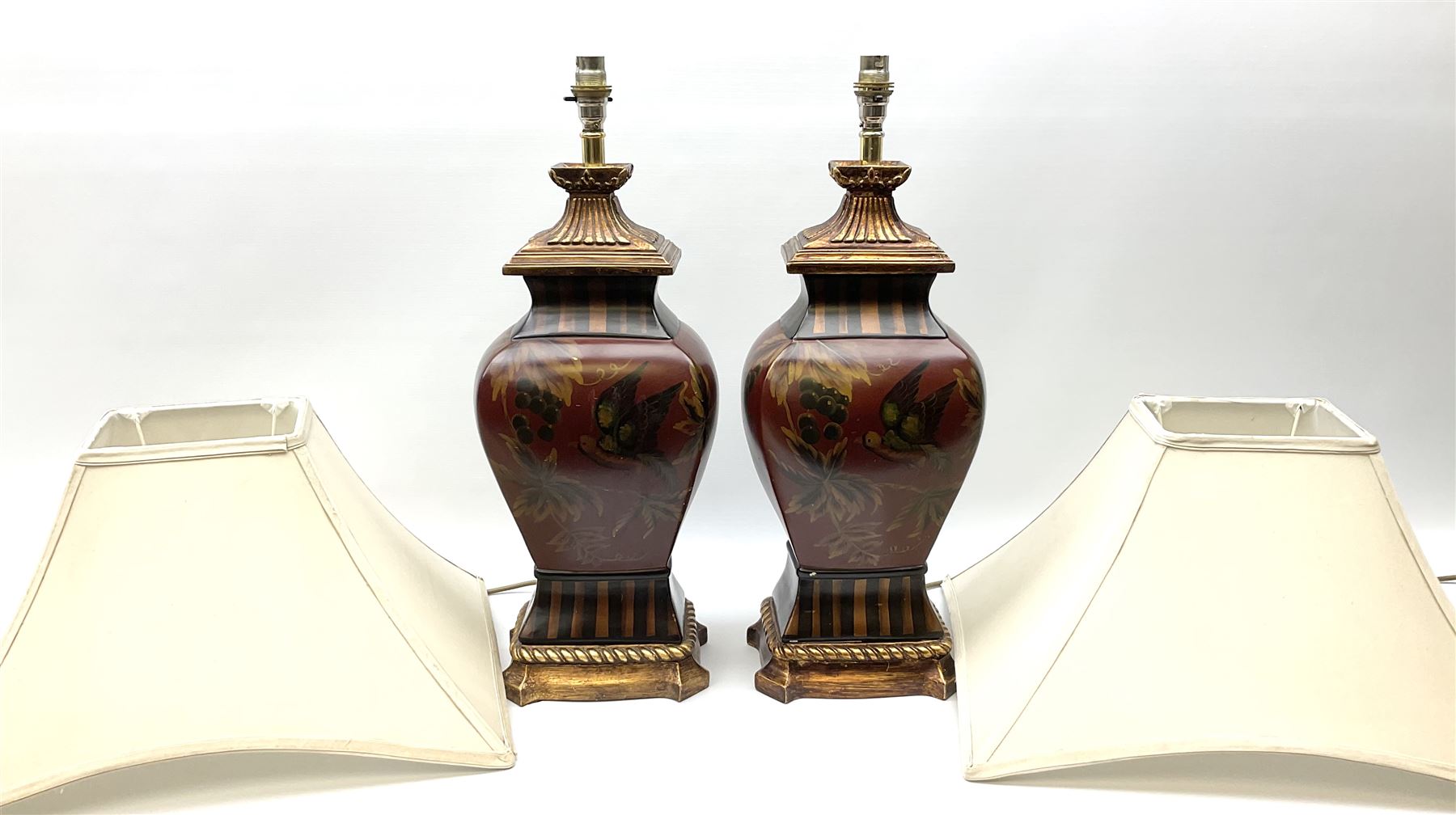 Pair Oriental table lamps decorated with birds in a tree with fruit, on a red ground with a gilded base together with cream lampshades H57cm, without lampshade. 