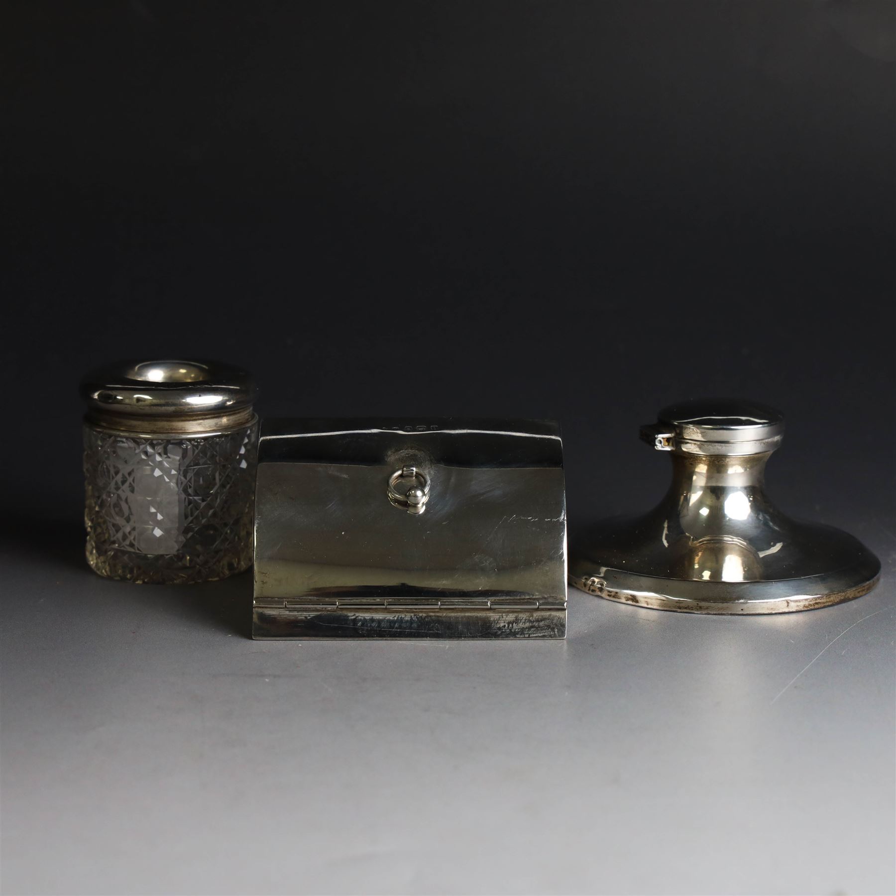 Edwardian silver fall-front ring box with loop handle, opening to reveal velvet interior with five ring spaces, hallmarked Deakin & Francis, Birmingham 1907, together with a cut glass jar with silver lid inscribed 'Hair Tidy' and a silver mounted capstan inkwell, both hallmarked 