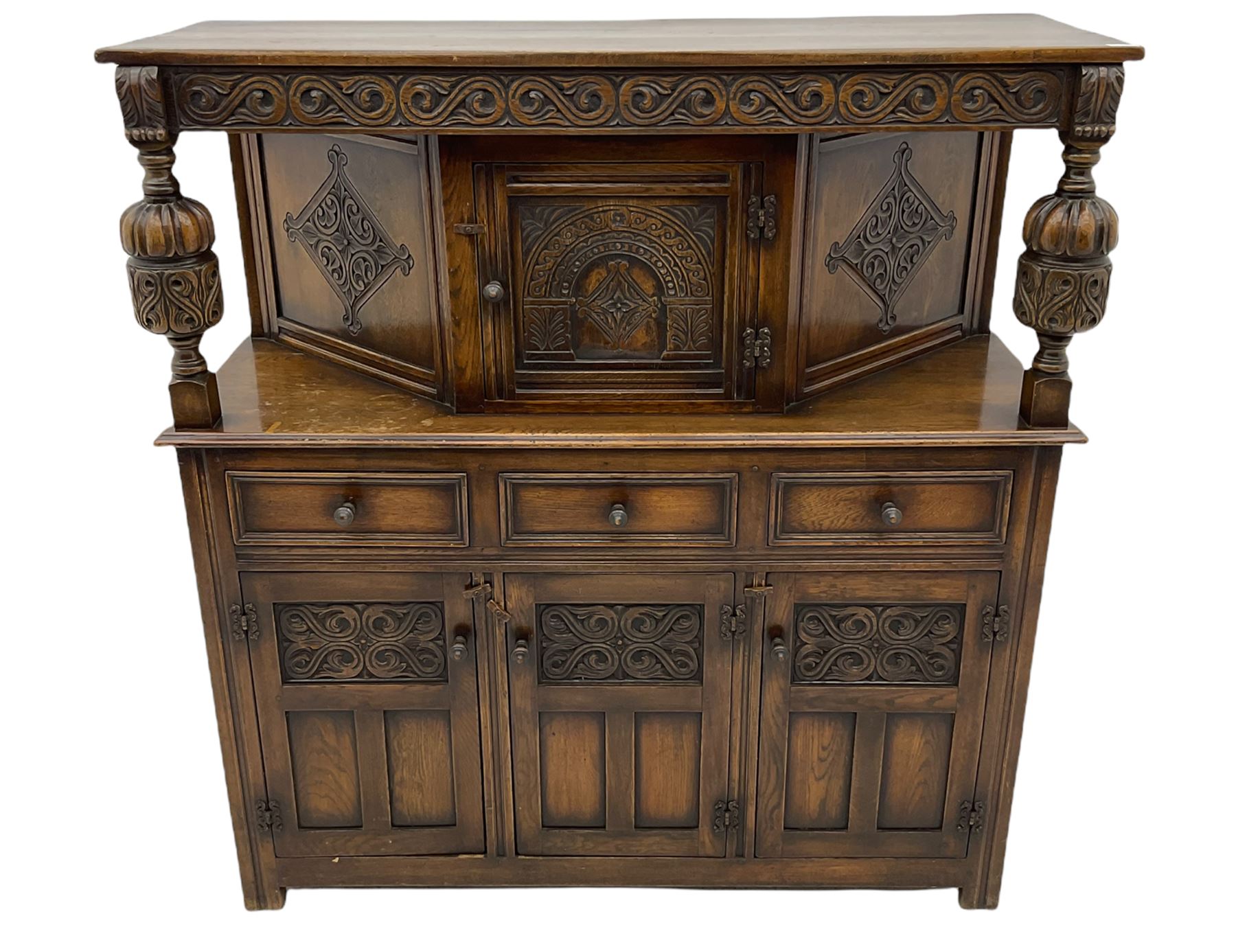 20th century carved oak court cupboard, s-scroll carved frieze over panelled cupboard door carved with arch, lobe and scroll carved cup and cover supports, fitted with three drawers and three cupboards below