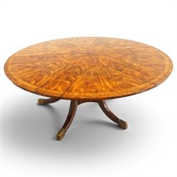 Theodore Alexander - Regency Revival figured mahogany 'Althorp Patent Jupe' extending dining table, the segmented circular top formed of six pull-out triangular divisions with inset fold-out leaves, raised on a large turned vasiform pedestal on a pentagonal platform base with ebonised stringing, terminating to five splayed supports with gilt metal acanthus scrolled feet, retailed by David Hick Interiors, Jersey