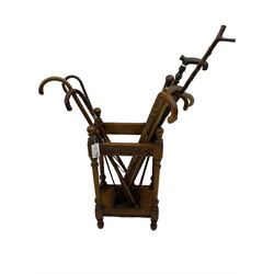 Early 20th century oak stick stand, rectangular structure with decorative carving, square base fitted with tray, on turned supports topped with finials; twelve assorted walking canes 