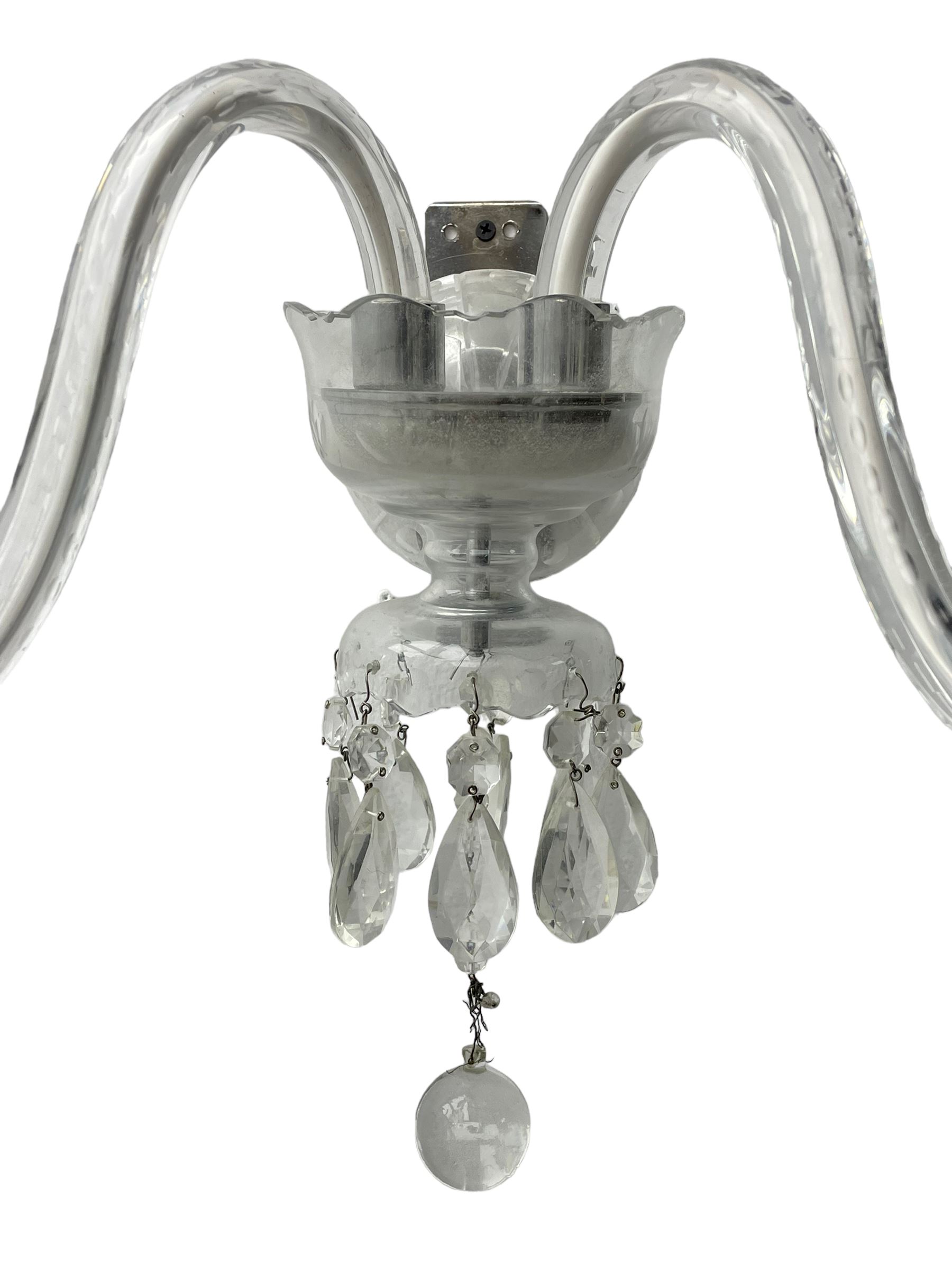 Pair of cut glass two branch wall sconce candelabras, each with S scroll extending branches with shaped and bevelled circular drip trays, hung with pendant drops