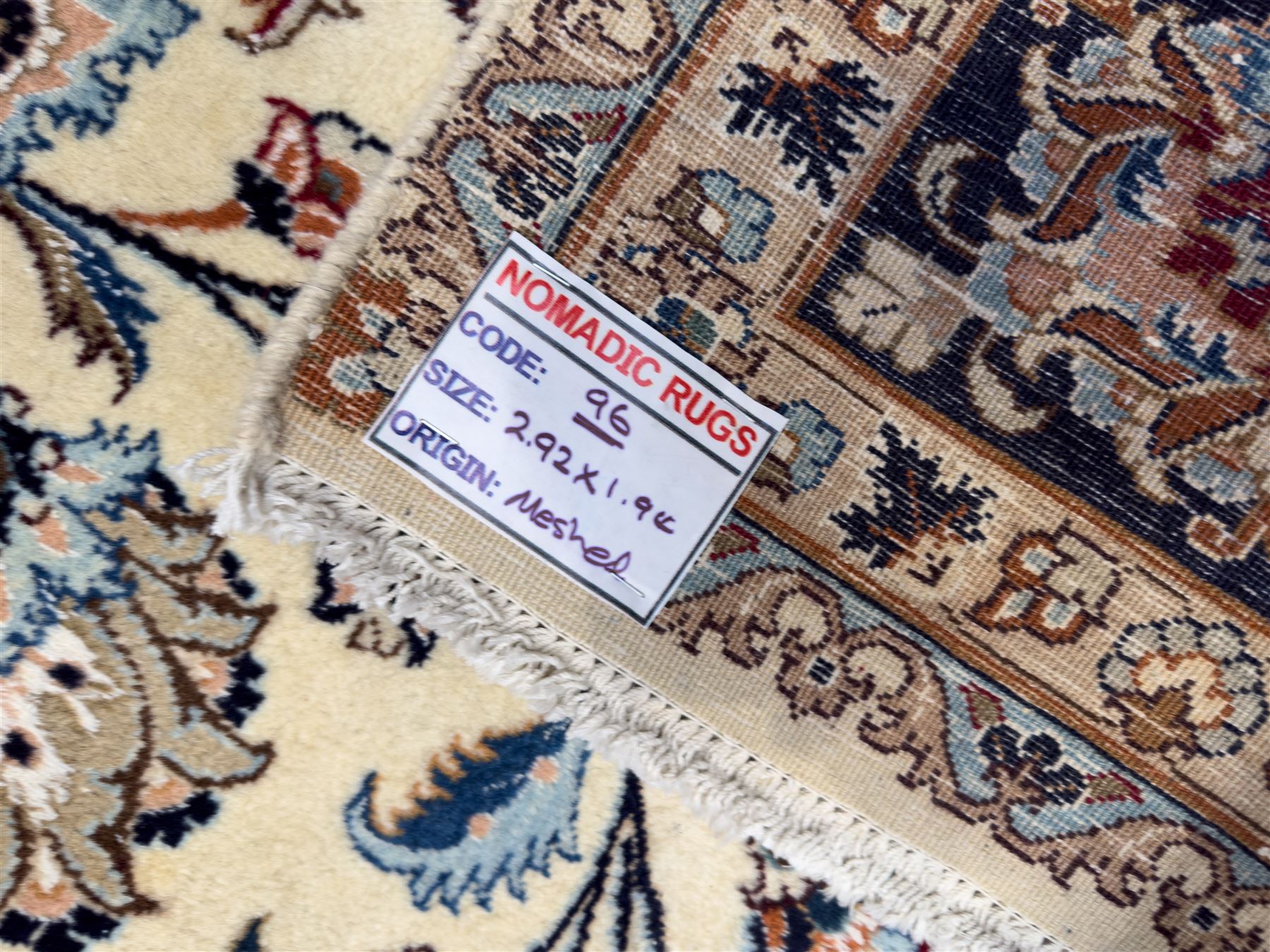 North East Persian Meshed hand-knotted rug, ivory field with scrolling vines, palmettes, and rosettes in shades of blue and brown, within a dark blue border of palmettes and flowerheads between multiple guard stripes, with cotton fringe ends  