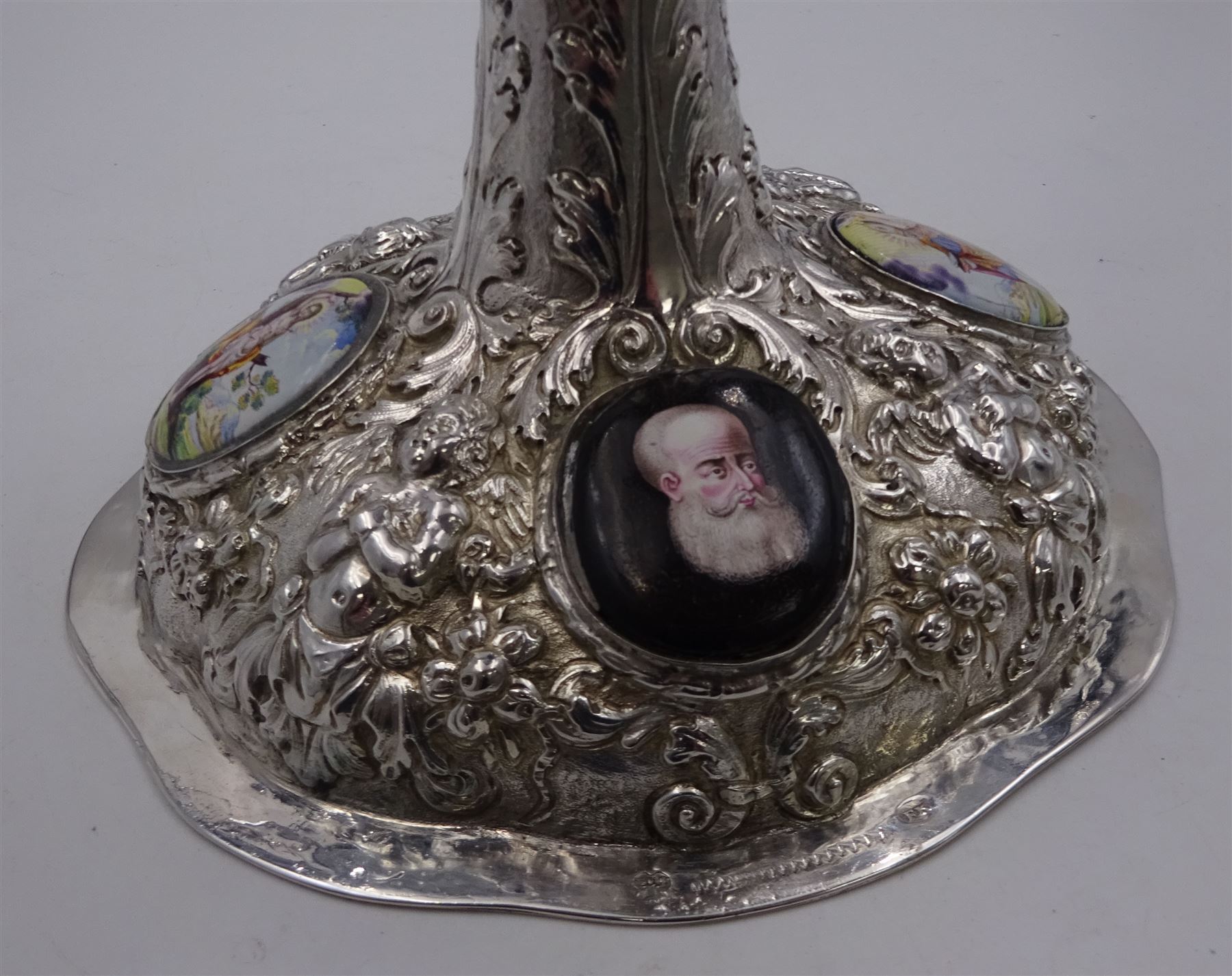 German silver chalice, the bowl, stem and foot each with 19th century repousse and chased decoration depicting putti masks, C scrolls and flowers, set with two hand painted porcelain roundels, possibly Berlin, and six later applied enamel roundels, each depicting religious scenes, the gilded bowl upon knopped stem and spreading octofoil foot, the base with marks for Munich, c.1695 and maker's mark FK
