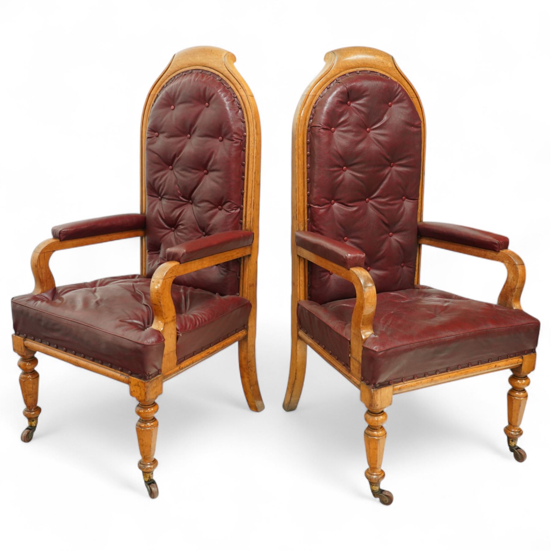 Impressive pair of mid-Victorian oak throne or hall chairs, arched backs on fluted supports with a deep buttoned upholstered panel and upholstered curved arms over fluted seat rails and tapering turned front legs with original brass and brown porcelain castors, and out-swept rear supports