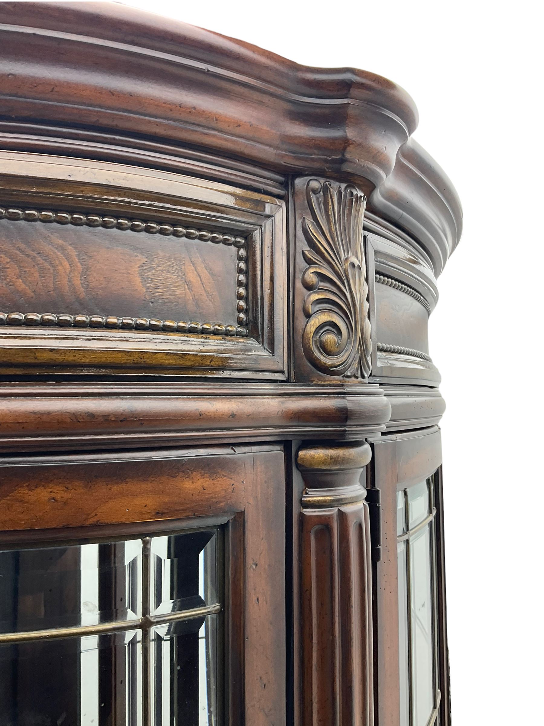  Kevin Charles American walnut demi lune display cabinet with illuminated interior, projecting cornice, two bevel edge glazed doors enclosing two adjustable shelves above single drawer and four cupboard doors with wine rack, carved scrolling supports