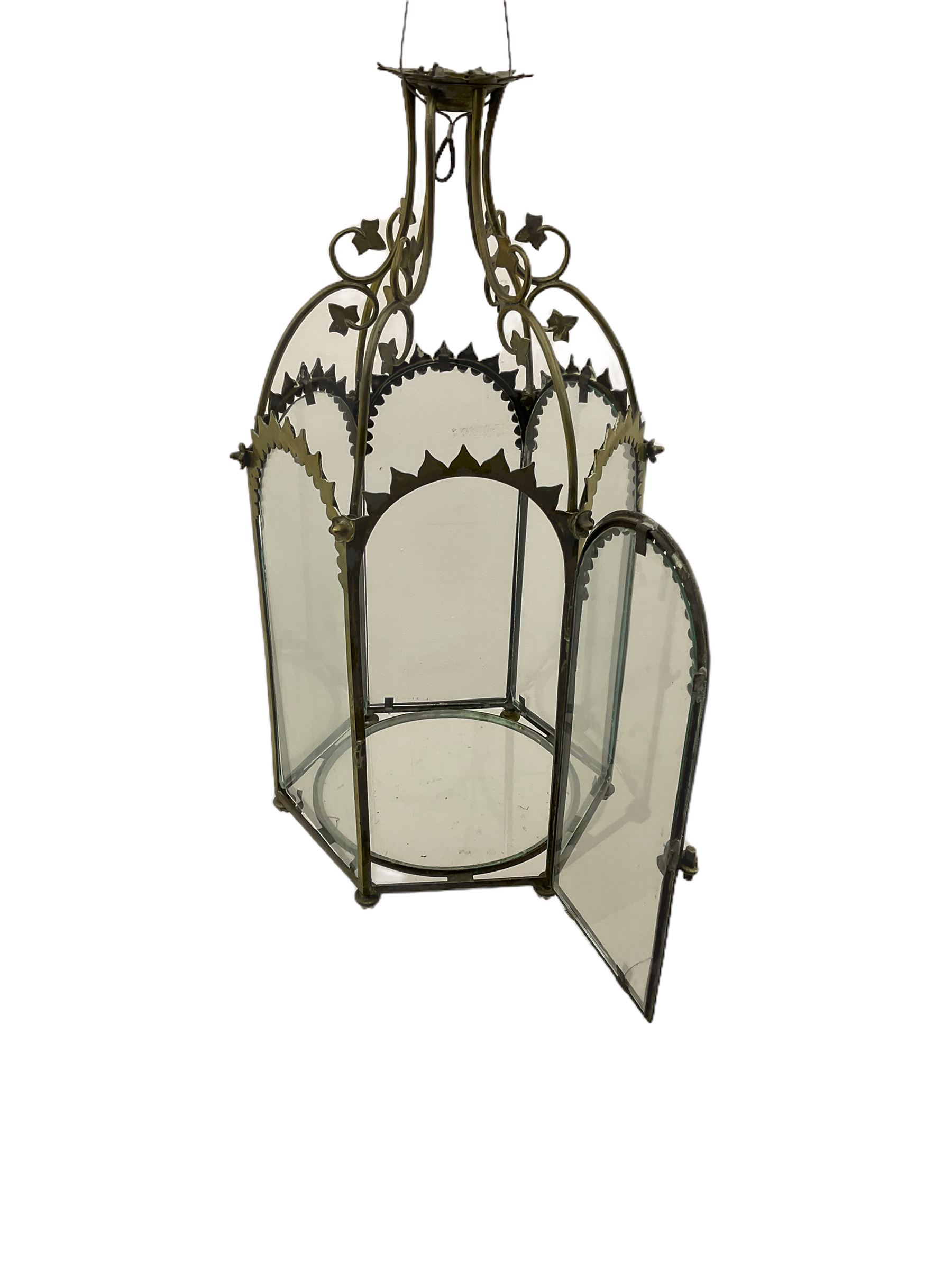 19th century brass and clear glass hexagonal hall lantern, with scrolling wire work open domed top over six arched panels, including a hinged door, the base enclosed with a circular glass panel on turned feet, H64cm