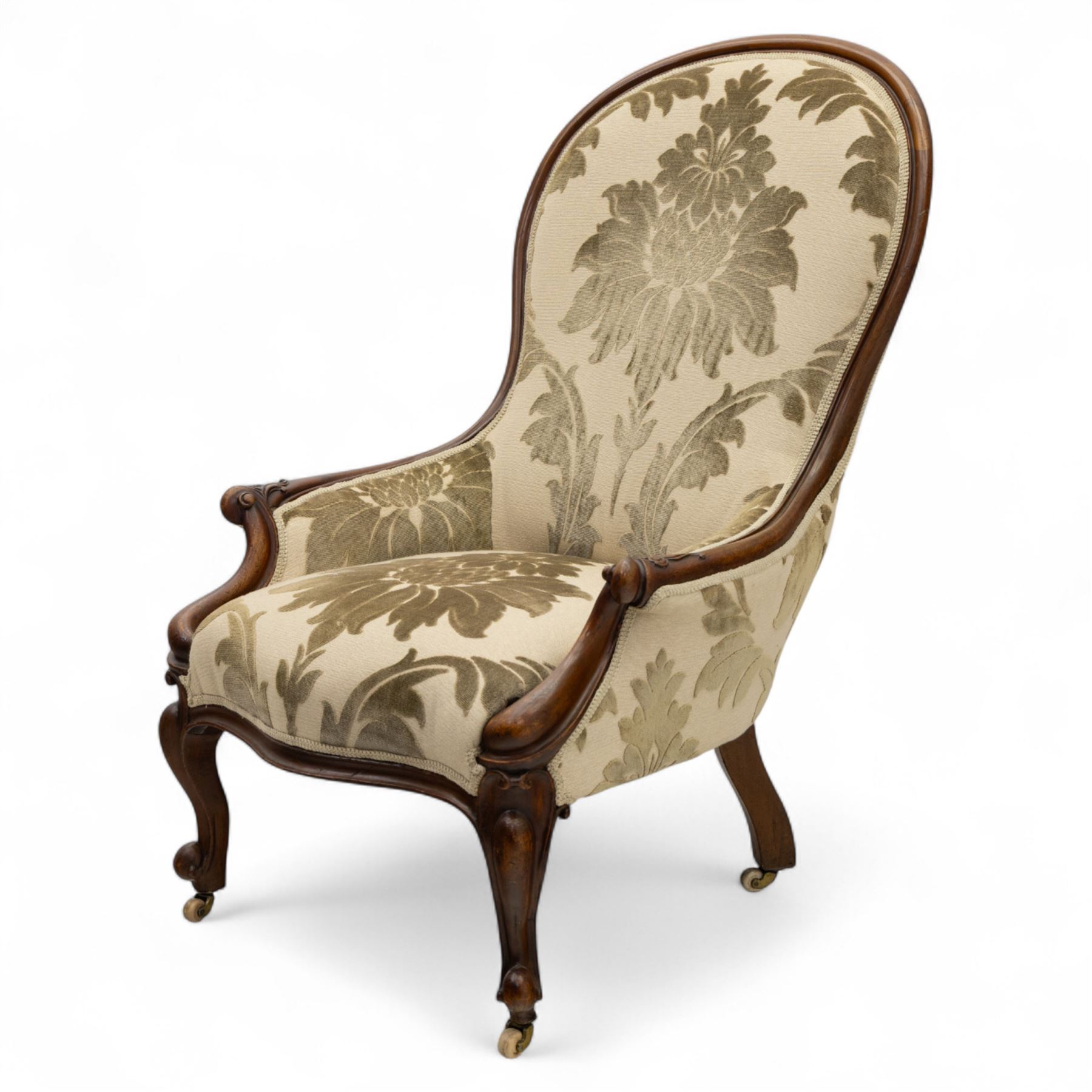 Victorian mahogany framed spoon back armchair, the shaped and padded back over serpentine seat upholstered in a floral damask pattern fabric within a moulded frame carved with scrolled arms, raised upon cabriole front legs with scroll feet on porcelain castors 