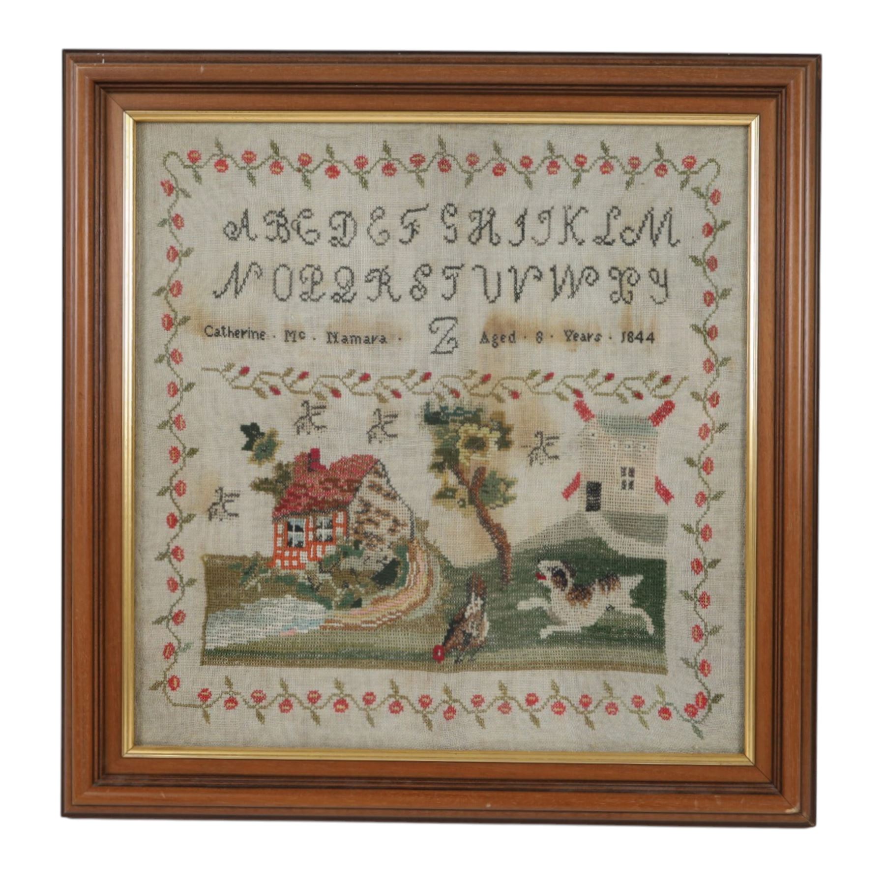 Mid 19th century sampler, by Catherine Mc Namara, Aged 8, and dated 1844, worked with alphabet band above a countryside scene with cottage, stream, windmill, chicken and dog, within a flowering vine border, including frame 51cm x 49.5cm