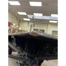 Large 19th century carved oak library table, the rectangular top with lunette carved edge over cartouche panelled and carved  scroll frieze, the central tapering rectangular support relief carved with masks and garlands, on four carved seated lion supports at each corner, on flat angular stretcher with recessed castors stamped ‘Bartholomew & Fletcher, London’