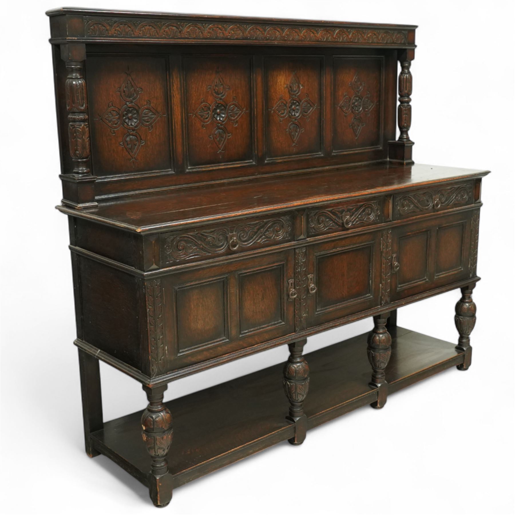 Early 20th century carved oak sideboard Jacobean style with panel back on cup and cover legs, the top section with carved panels and reeded moulding, three deep frieze drawers over triple panelled cupboard doors, raised on carved baluster legs joined by lower shelf