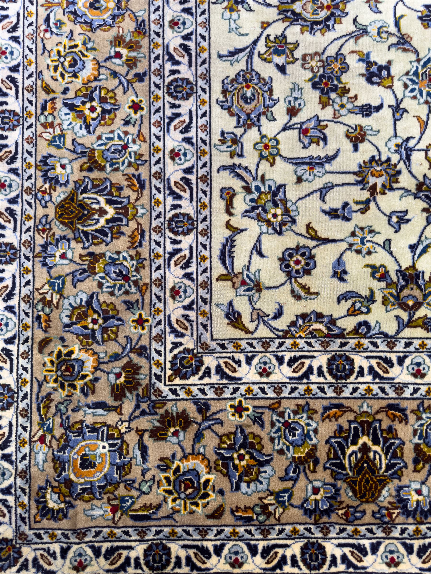 Central Persian Kashan hand-knotted carpet, ivory field with an all-over design of scrolling vines, lotus palmettes, and rosettes in shades of blue, gold, and brown within a blue ground border of palmettes and arabesques between multiple guard stripes