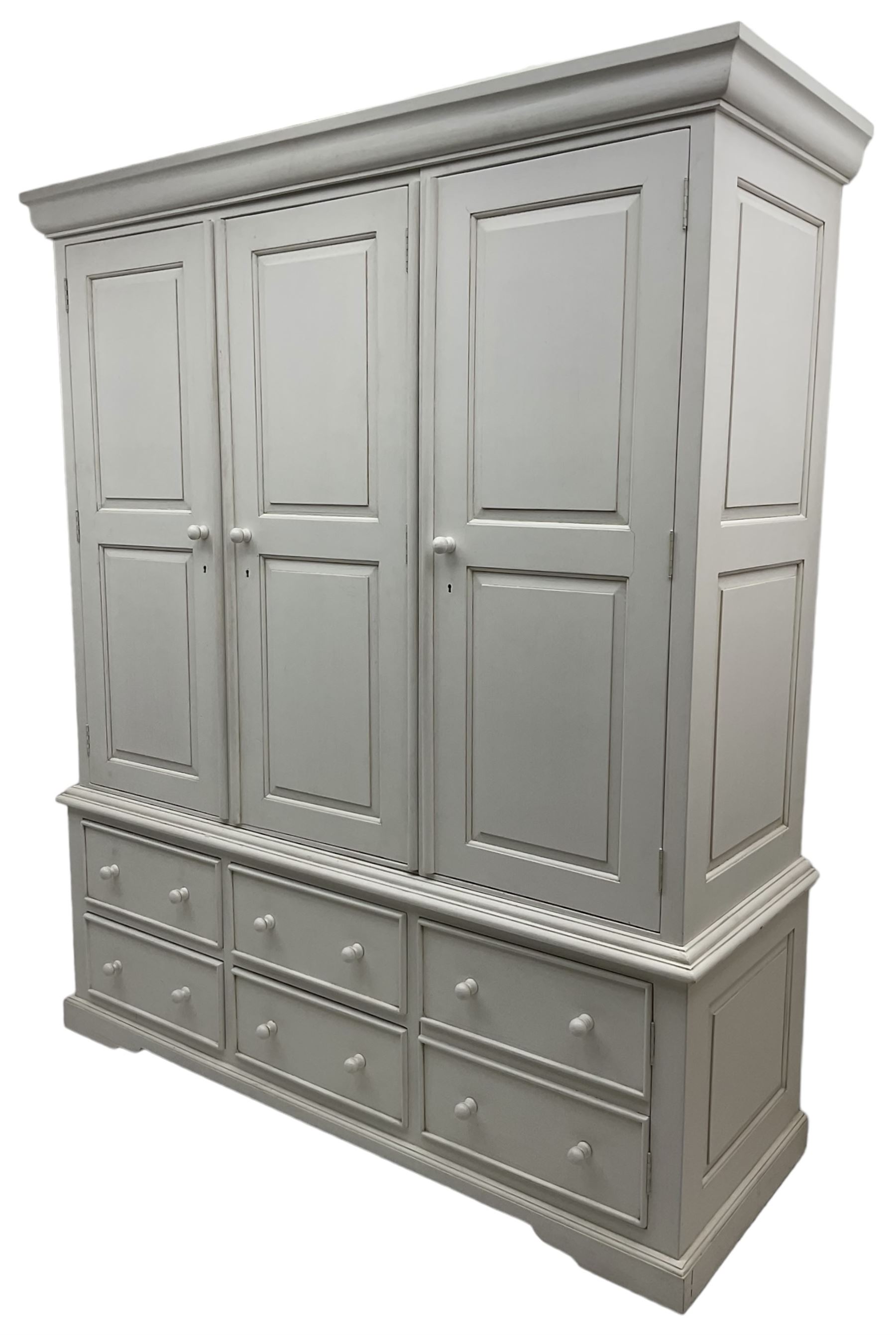 White painted triple wardrobe, projecting moulded cornice over three panelled doors, the interior fitted with hanging rails, four drawers and hinged cupboard to base, on bracket feet