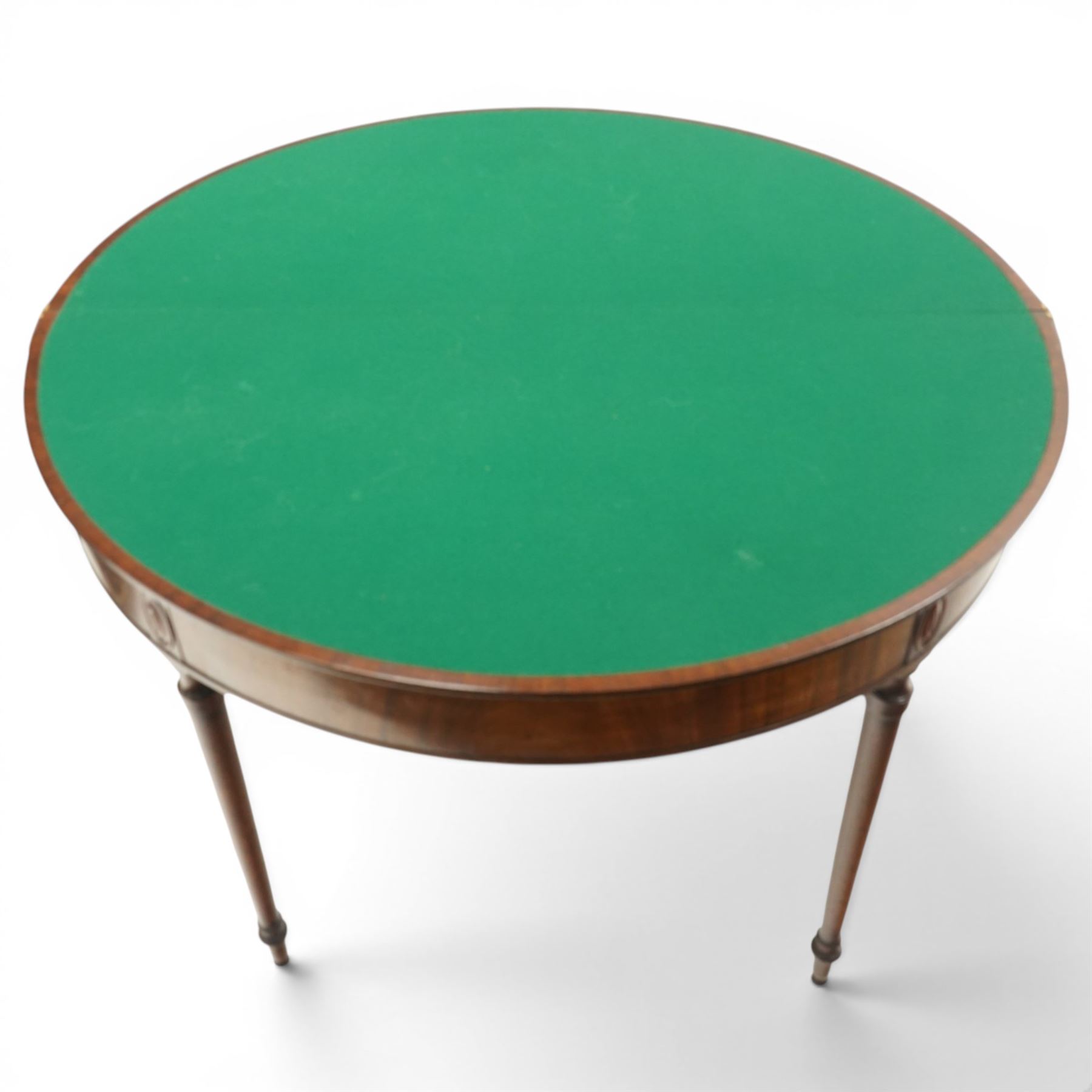 Georgian mahogany demi-lune card table, the lunette shaped top with cross-banded and boxwood-strung edge, opening to reveal baize-lined interior and supported by rear gatelegs, over a banded frieze with applied oval plaques, raised on turned and tapering supports