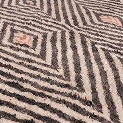 Moroccan Berber hand-knotted rug, of rectangular form, ivory ground decorated with bold, repeating lozenge motifs defined by alternating charcoal grey linear bands, with a striking geometric lattice and chevron with diamond designs, enclosing smaller stylized devices in soft blush tones, with fringe ends