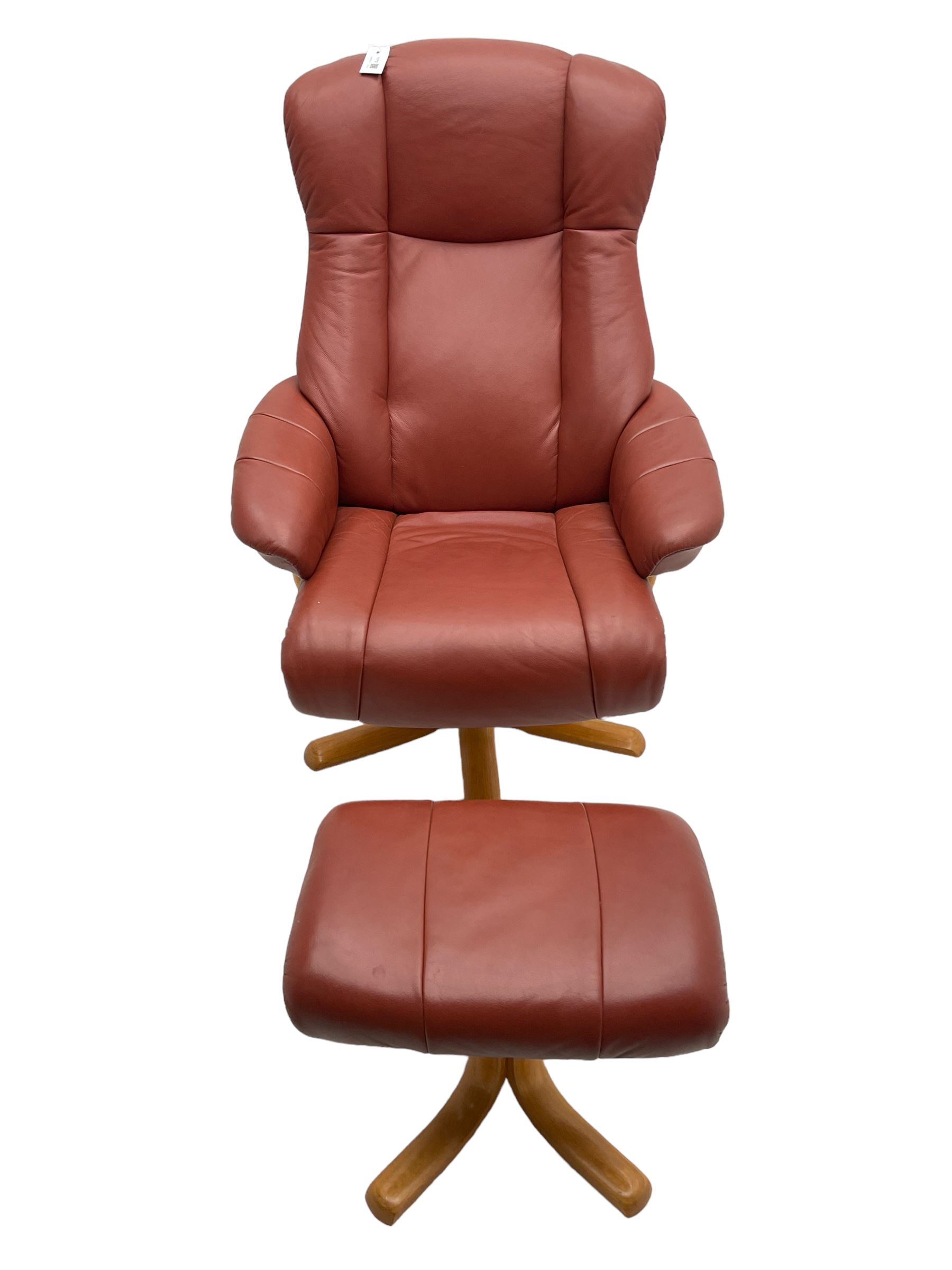 Mid-20th century design reclining armchair with swivel action, upholstered in red leather, raised on U-shaped supports with quadruform base, with matching footstool