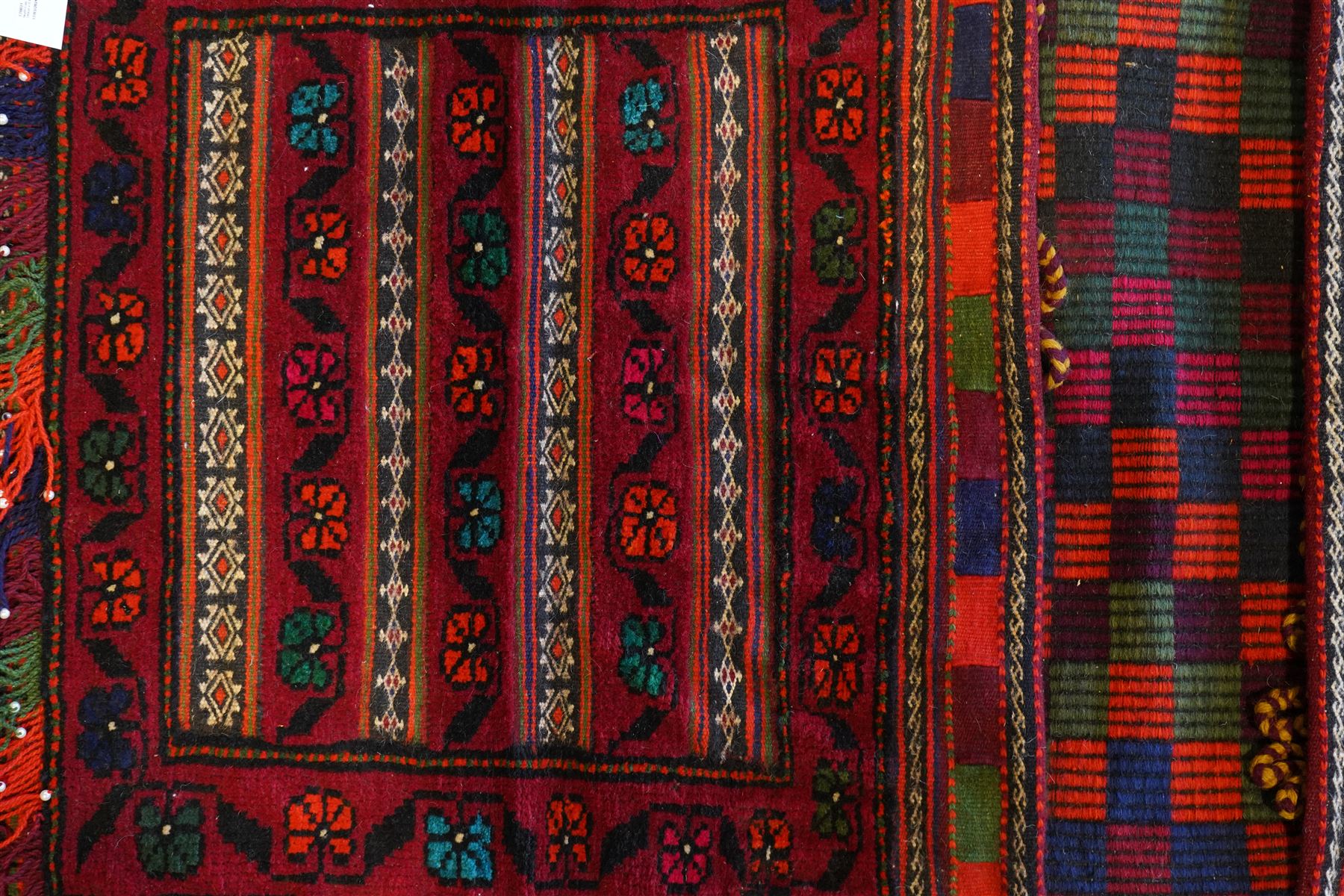 North East Persian Turkoman saddle bag, traditional double pouch form, each panel with madder red ground, decorated with horizontal bands of stylized geometric floral motifs and angular vine work, framed simple borders, central panel woven in flatweave with polychromed chequered design flanked by braided carrying cords with tasselled and knotted decorative elements 