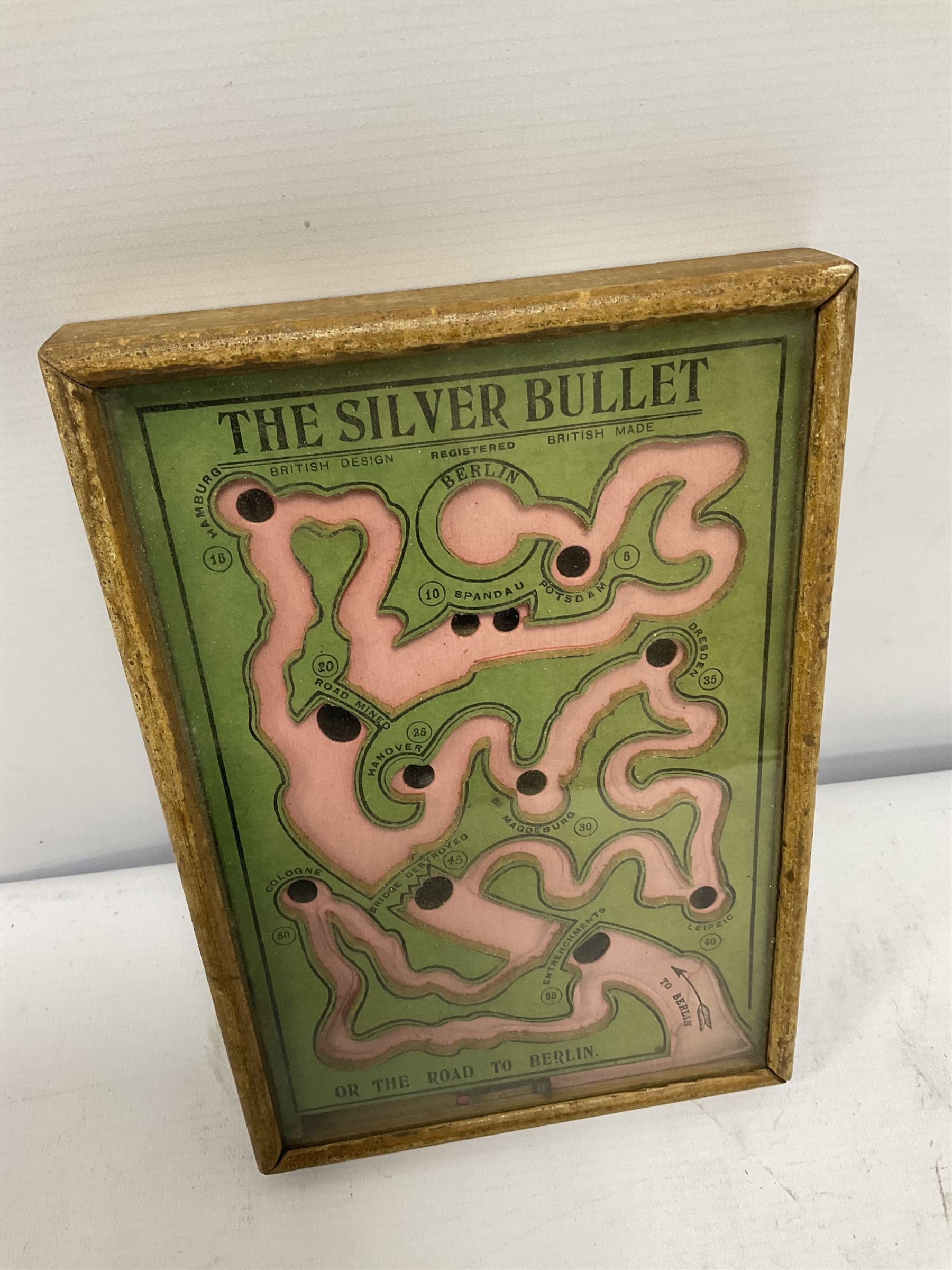WWI 'The Silver Bullet or the Road to Berlin' ball bearing puzzle game, the stylised printed card map marked with various German towns and hazards on the allied advance to Berlin passing through towns and cities such as Hamburg and Dresden, manufactured by R. Farmer and Son circa 1916, with instructions label verso, in glazed frame