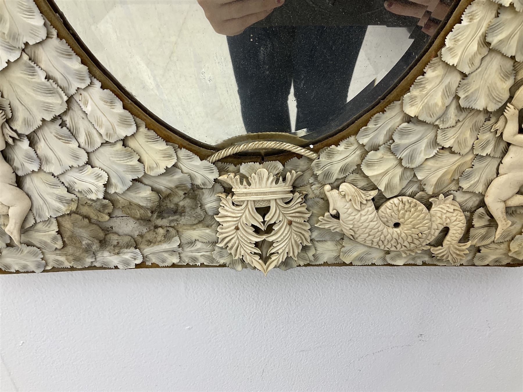 Pair 19th century French Dieppe bone and ivory wall mirrors, the oval bevelled mirror plates within rectangular frames with shaped tops, profusely decorated with ivory leaves, further detailed with carved bone armorial type crest inscribed 'SGOTORVM', putti, fish and mask heads, H81cm W48cm