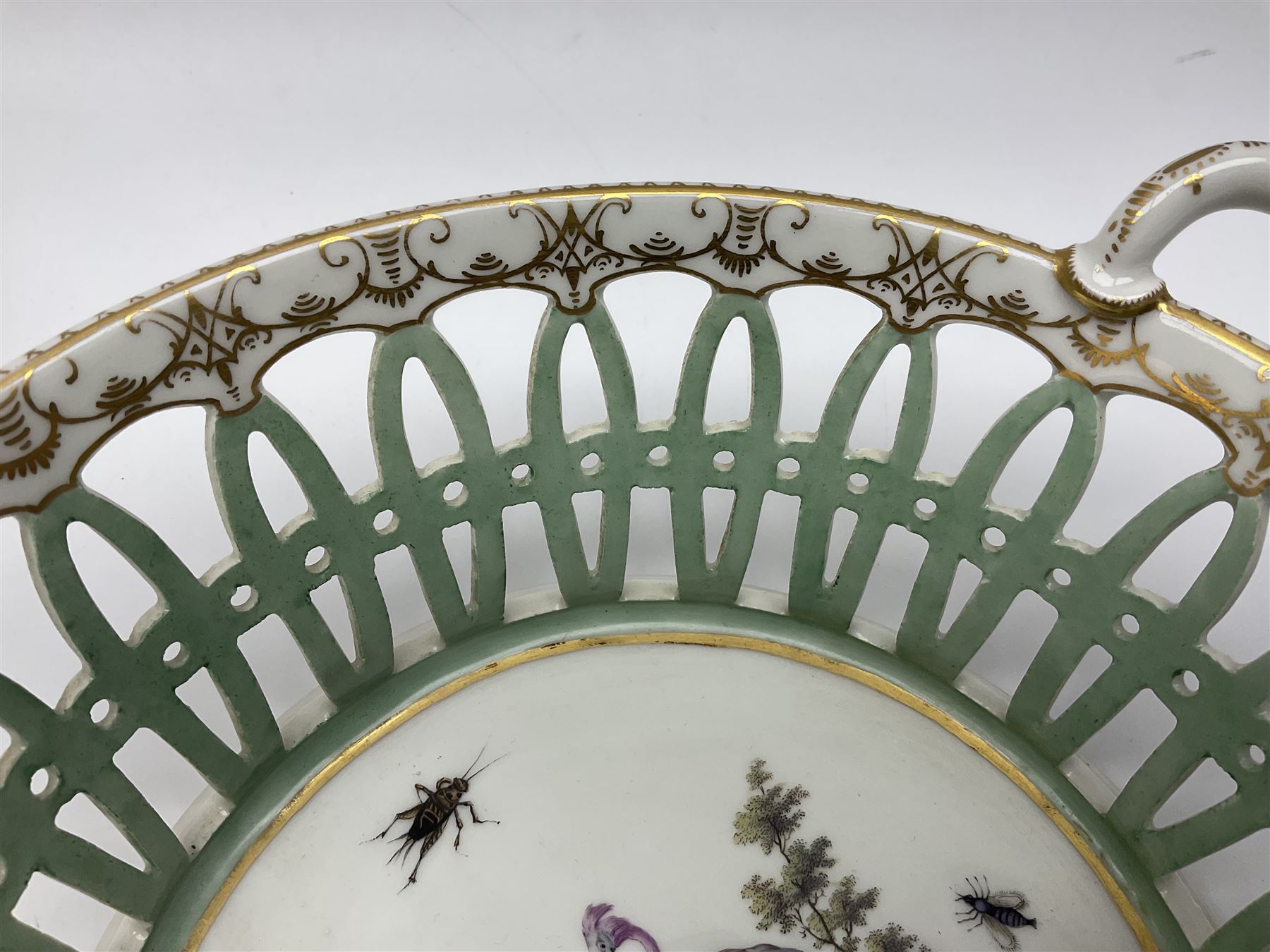 Pair of 19th century German openwork chestnut baskets, with twin handles and scrolling gilt border and star rim, painted to the centre with birds and insects, D22cm 