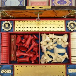 19th century walnut and brass bound games compendium box, painted to enhance the grain, of rectangular form, the hinged opening cover with rounded sides, central brass cartouche with engraved lion crest, and brass riveted straps, opening to reveal a red leather and blue silk lined compartmented interior, with fold-down games board, and lift-out tray containing playing cards, ebony turned dice towers, white and red stained bone draughts, and chess pieces, ivory dice, and ivory and ebony whist markers, and brass bezique board, cribbage board and markers, H15cm W32cm D24cm
This lot has been registered for sale under Section 10 of the APHA Ivory Act