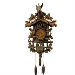 A large and imposing 20th century three train 30hr cuckoo clock with automata and musical features, profusely carved case with a carousel, animals, leaves and sporting guns, dial with pierced wooden numerals and wooden hands, with three weights and pendulum, strike/silent facility. 
