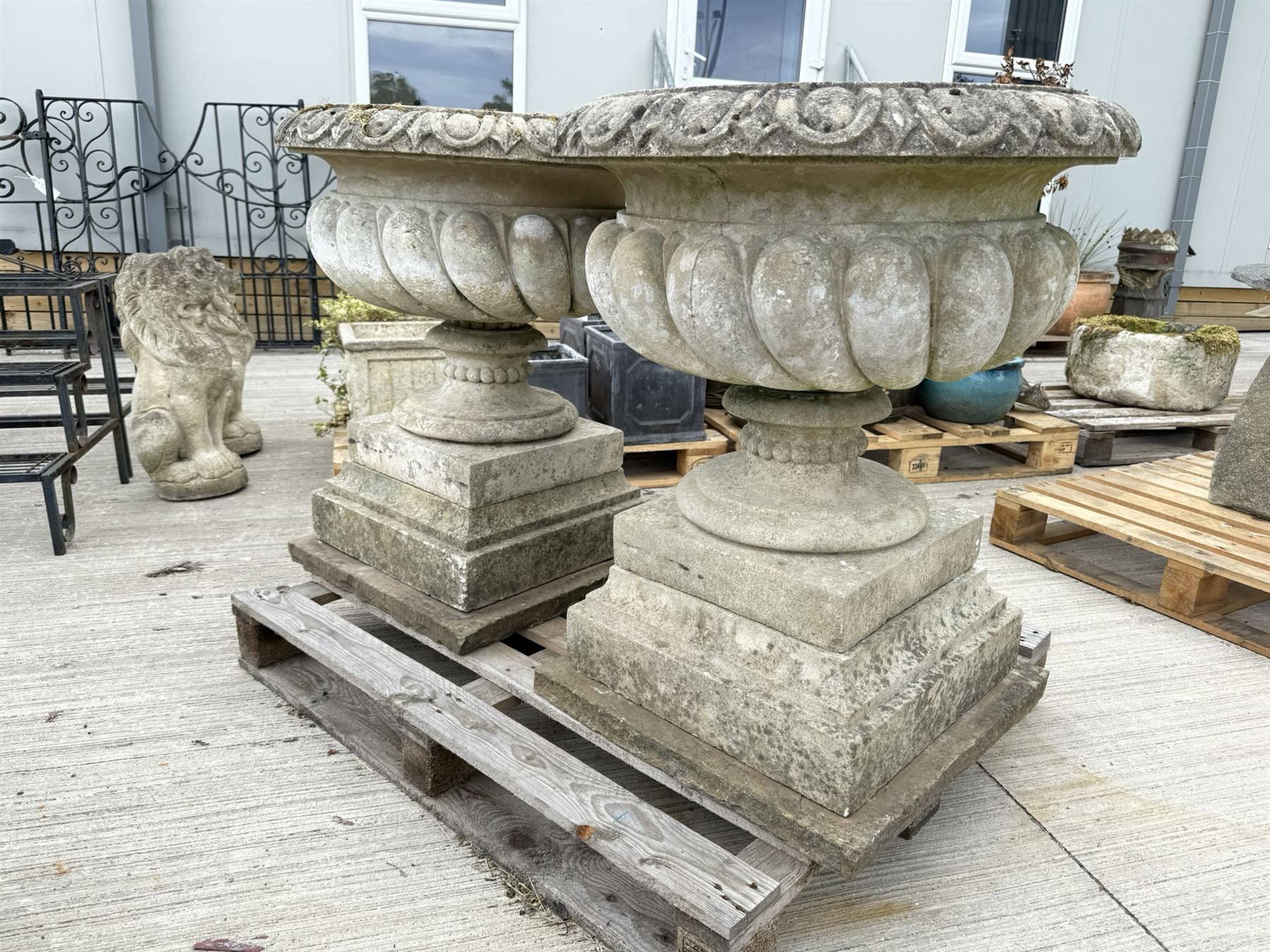 Pair of large weathered Country House Haddonstone garden urns, acanthus carved rim above gadrooned bowl, beaded detailing to the neck, raised on stepped double plinth base
