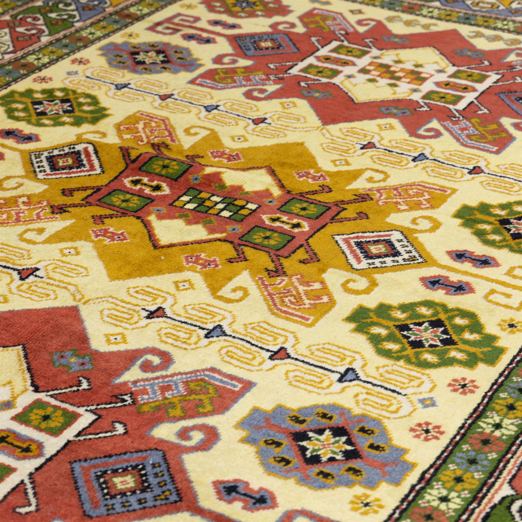 Caucasian Kazak design wool rug, cream field with three large geometric medallions and stylised hooked motifs, enclosed by polychrome reciprocal border and green floral guard stripes