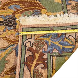 Arts & Crafts design wool pile rug, decorated with repeating stylized floral seed-head motifs and scrolling foliage within a complementary floral border in a muted palette of green, ochre, blue, and brown, with cotton fringe ends, with label for London House Oriental Rugs & Carpets  
